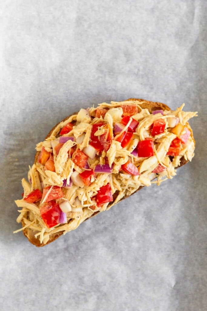 A piece of toasted sourdough bread with chicken salad on top of it on a piece of parchment paper.