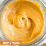 Overhead shot of chipotle mayo in a jar. Next to the jar is a striped towel, a spoon with mayo on it, and a teaspoon.