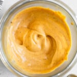 Overhead shot of chipotle mayo in a jar. Next to the jar is a striped towel, a spoon with mayo on it, and a teaspoon.