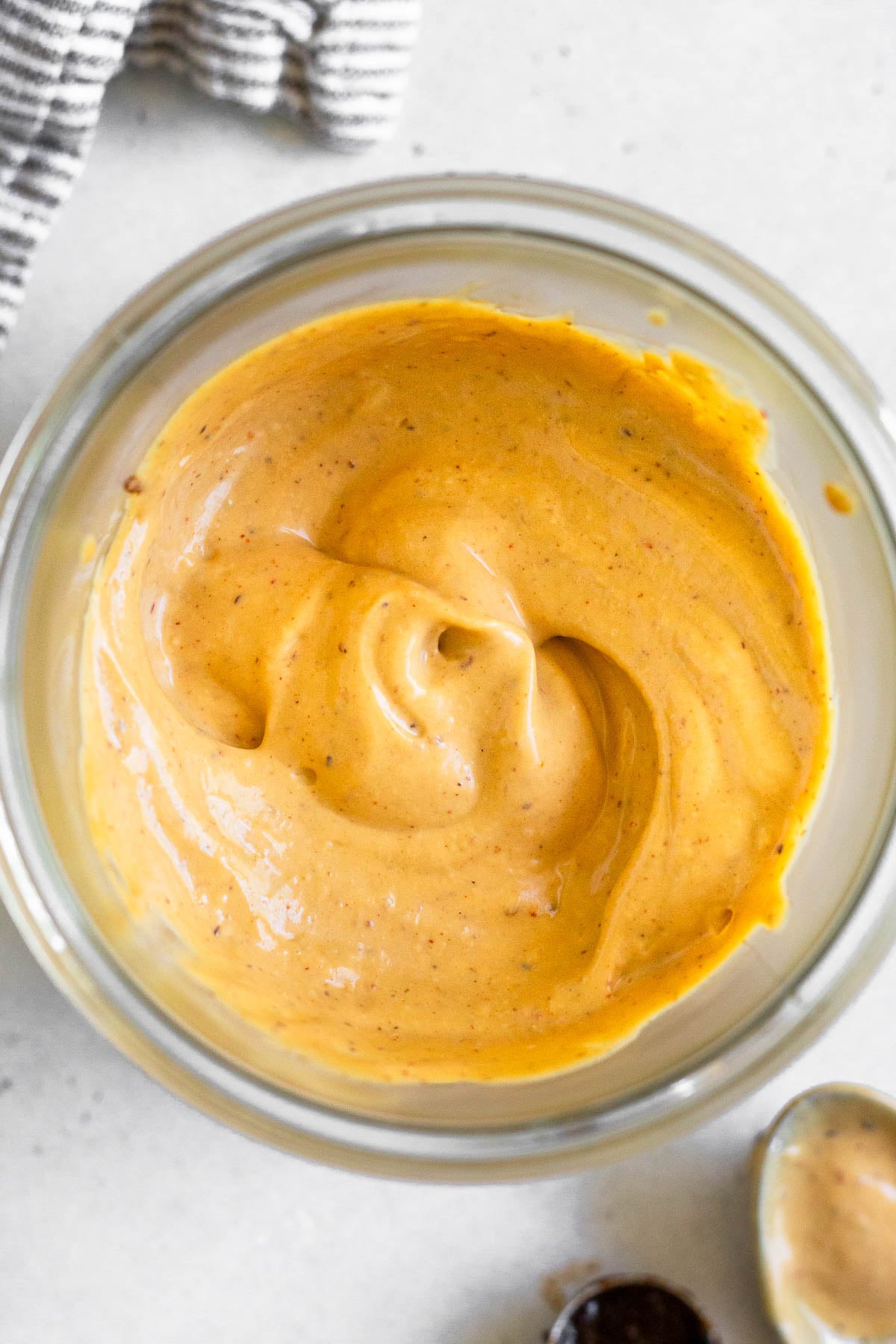 Overhead shot of chipotle mayo in a jar. Next to the jar is a striped towel, a spoon with mayo on it, and a teaspoon.