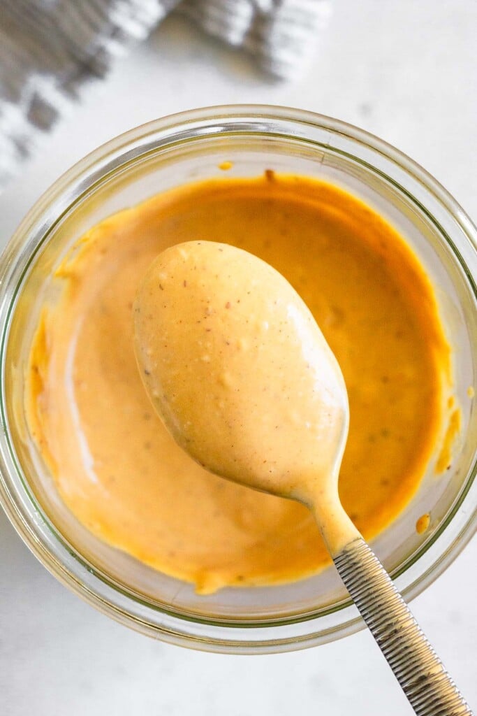 A spoonful of chipotle mayo being scooped out of a jar. Next to the jar is a striped towel.