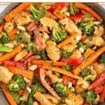 High protein chicken recipe in a skillet with chicken breasts, bell peppers, and broccoli tossed in a peanut sauce. It is topped with sesame seeds, peanuts, and fresh cilantro.