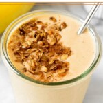 Peanut butter banana protein smoothie in a glass jar topped with granola and cinnamon with a straw in it.