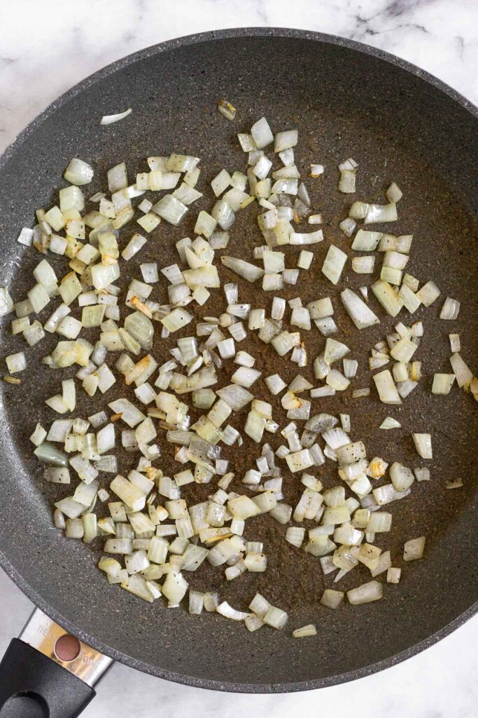 Large skillet filled with sautéed diced onions.