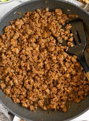 Ground beef taco meat in a large skillet with a spatula in it. The pan is sitting on a striped towel.