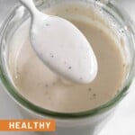 Healthy coleslaw dressing in a jar with a spoon full of dressing overtop of it. In front of the jar is half a juiced lime.