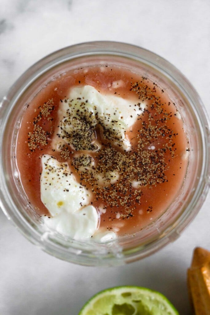 Overhead shot of a jar with greek yogurt, lime juice, red wine vinegar, and spices in it before it is mixed together. Next to it is half a juiced lime and a reamer.