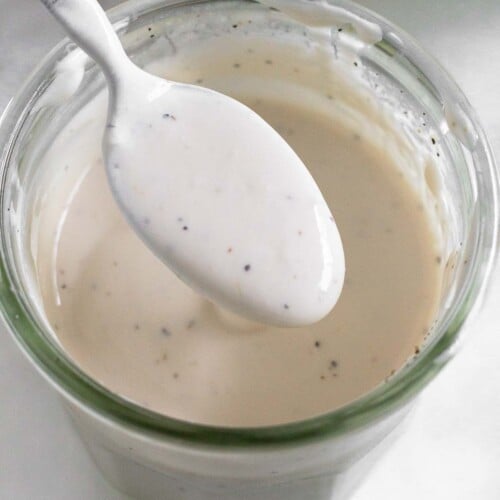 Healthy coleslaw dressing in a jar with a spoon full of dressing overtop of it. In front of the jar is half a juiced lime.