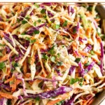 A closeup of a large bowl of healthy coleslaw garnished with fresh cilantro and black pepper.