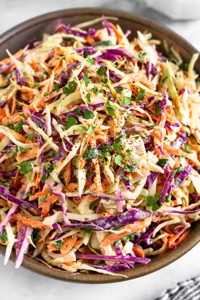 A large bowl filled with greek yogurt coleslaw. It is garnished with cilantro and black pepper.
