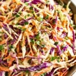A closeup of a large bowl of healthy coleslaw garnished with fresh cilantro and black pepper. A striped towel is in front of the bowl.
