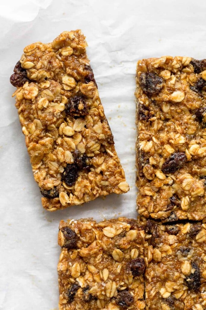 Overhead shot of oatmeal raisin granola bars lined up on parchment paper with one bar pulled slightly away from the other bars.