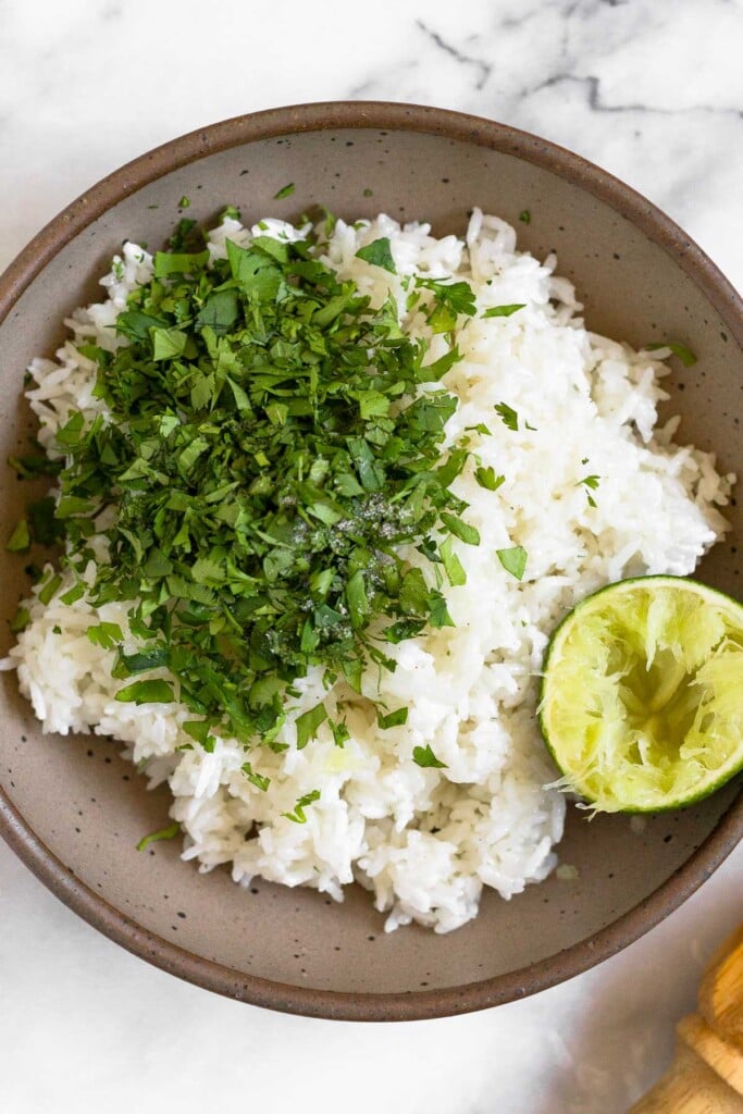 Large bowl bowl filled with rice rice with a bunch of chopped cilantro on top of it. Also in the bowl is half a juiced lime.