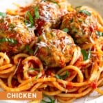 A bowl of zucchini meatballs on top of pasta mixed with marinara sauce. They are garnished with fresh basil and grated cheese.