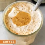 A jar of coffee overnight oats topped with yogurt, cashew butter, and cinnamon with a spoon in the jar. Behind it is another jar of overnight oats and bottle of cold brew coffee. In front of the jar is a teaspoon of cinnamon and some coffee beans.