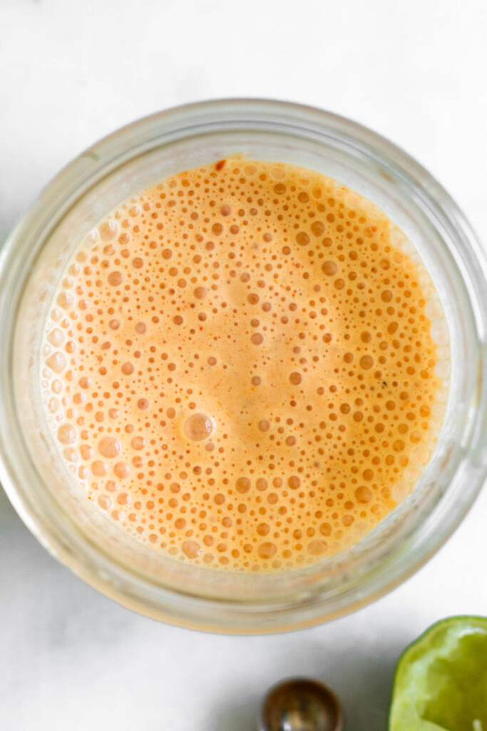 Overhead shot of salsa salad dressing recipe in a glass jar. Next to the jar is half a juiced lime and an empty teaspoon.