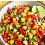 Mango cucumber salsa in a white bowl garnished with two lime wedges.