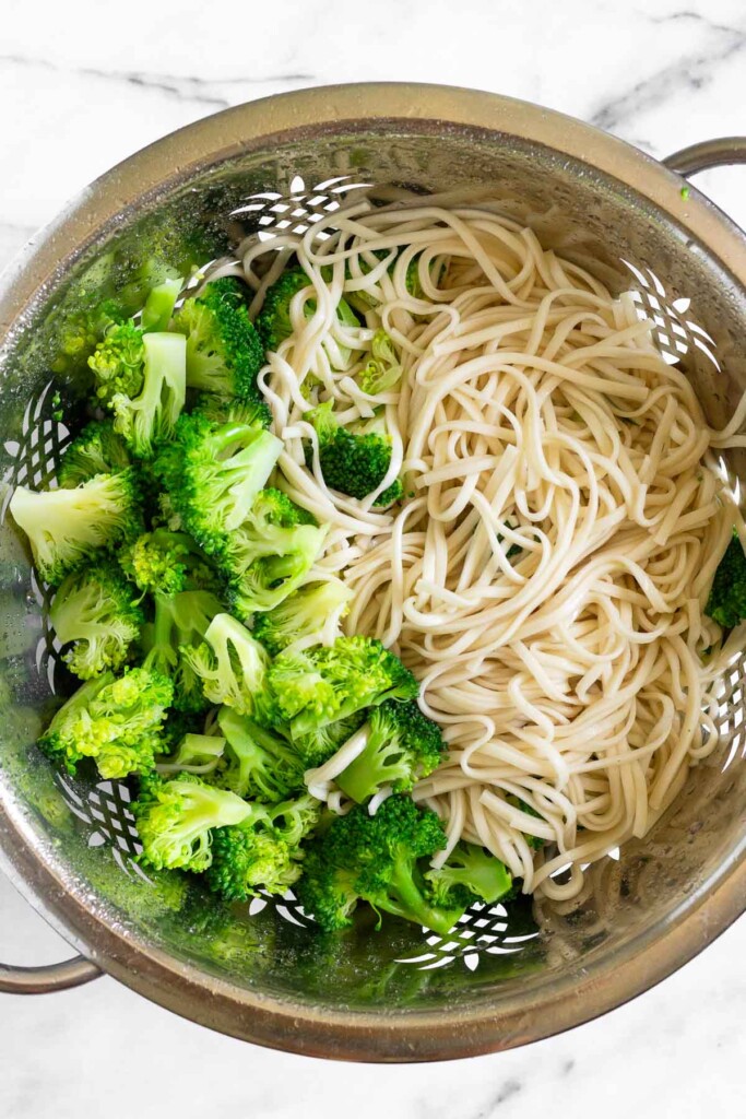 Overhead shot of a colander with cooked noodles and broccoli in it.