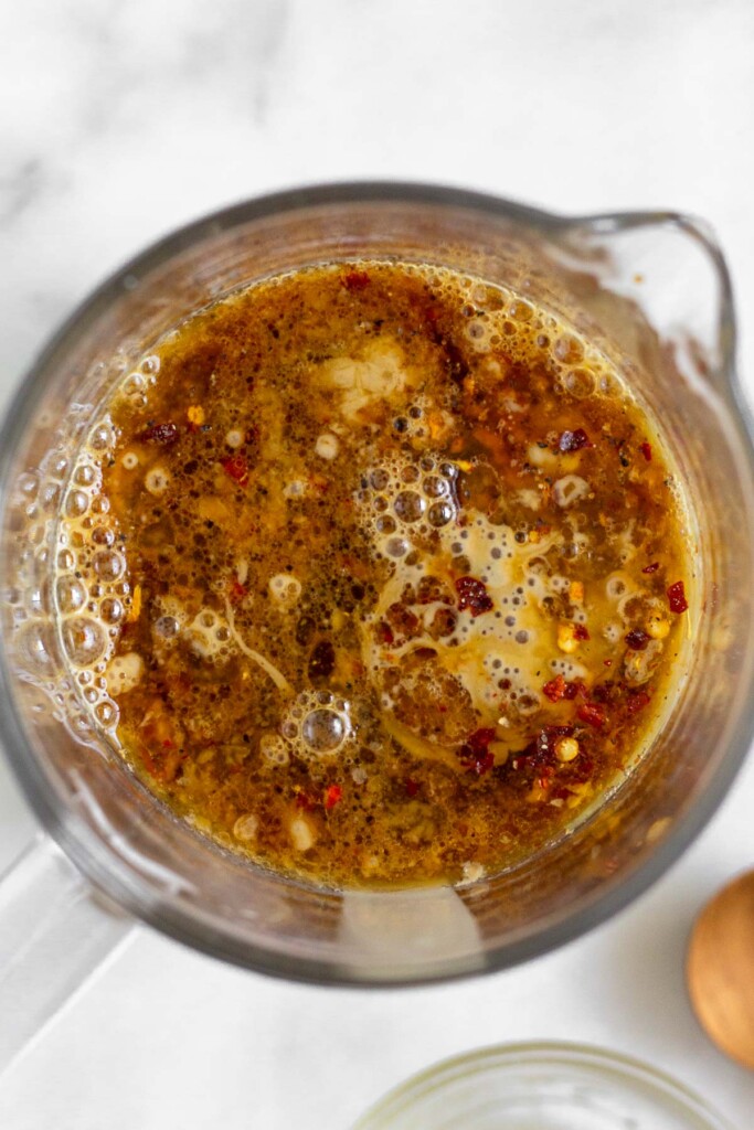 Measuring cup with tahini, coconut aminos, water, and spices in it before it is mixed together.
