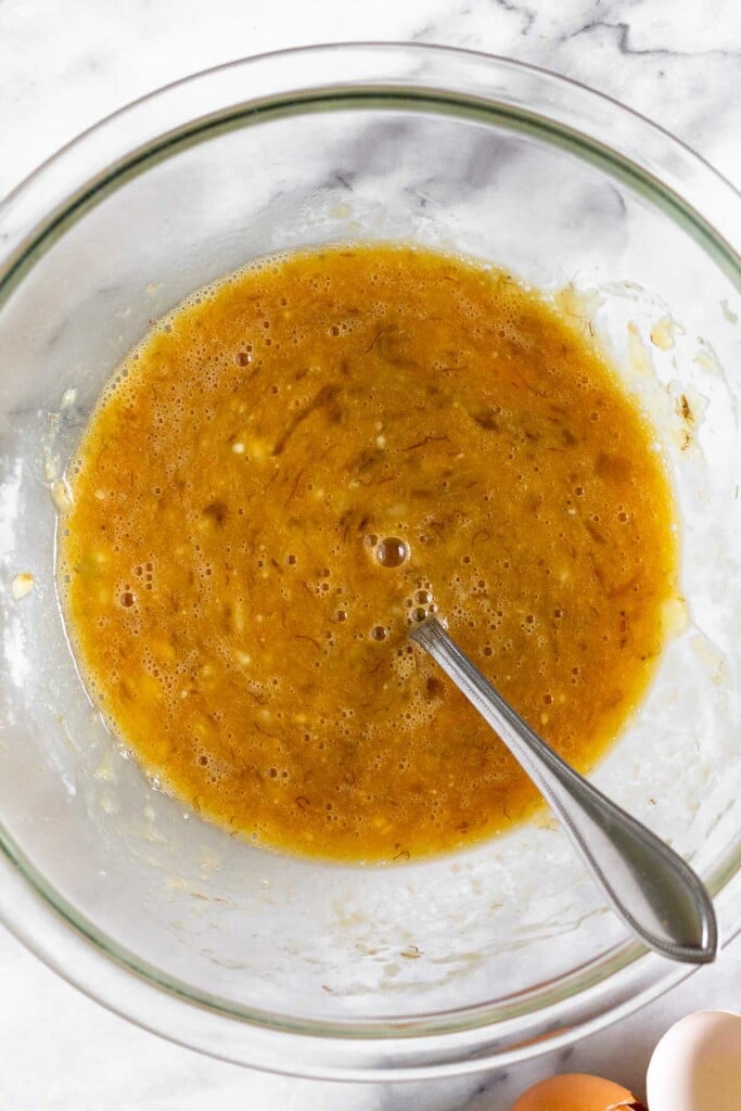 A glass bowl with a wet batter with a fork in it. Next to the bowl are two brown egg shells.