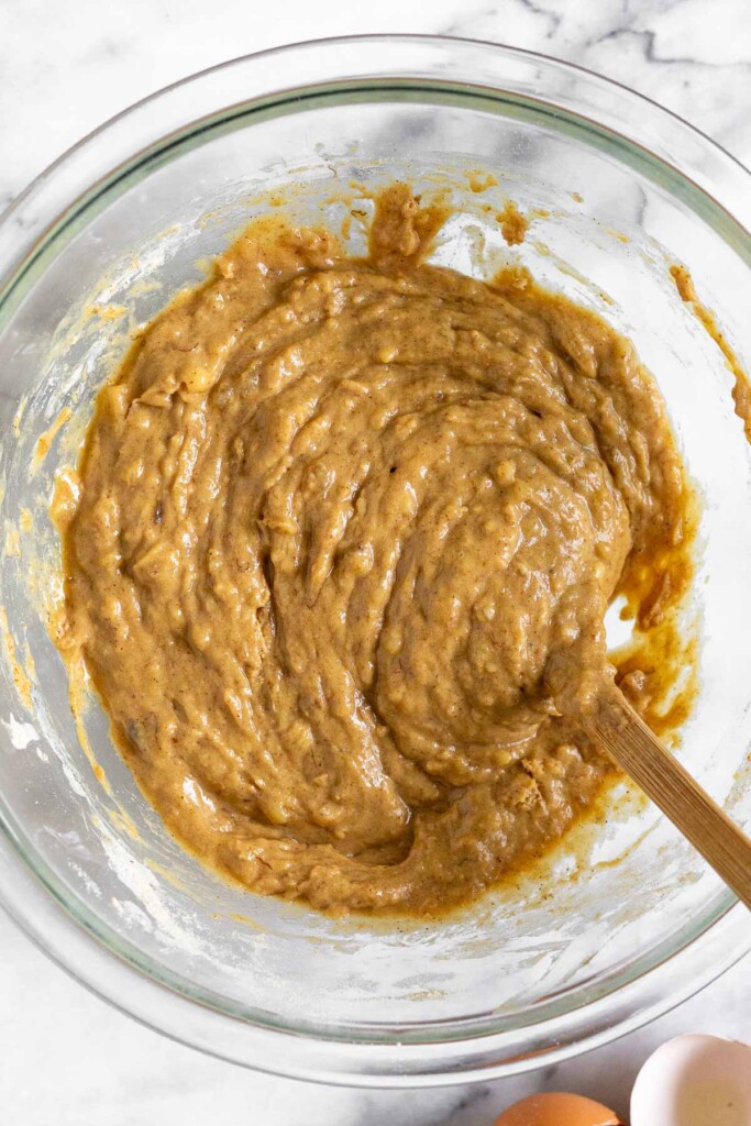 A glass bowl with a batter with a spatula in it. Next to the bowl are two brown egg shells.