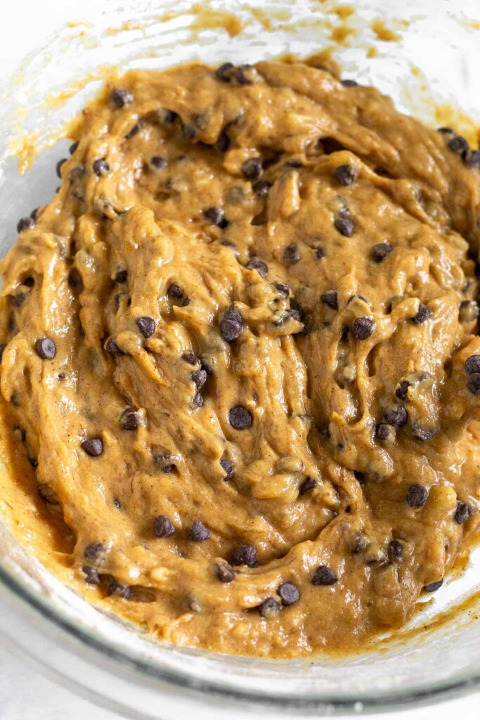 A close up shot of muffin batter with mini chocolate chips in a glass bowl.