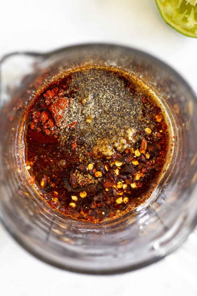 Measuring cup filled with coconut aminos, lime juice, minced garlic, and spices. Next to it is half a juiced lime.