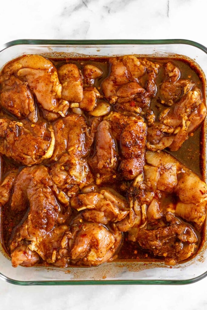 Glass dish with chicken thighs sitting in a marinade.