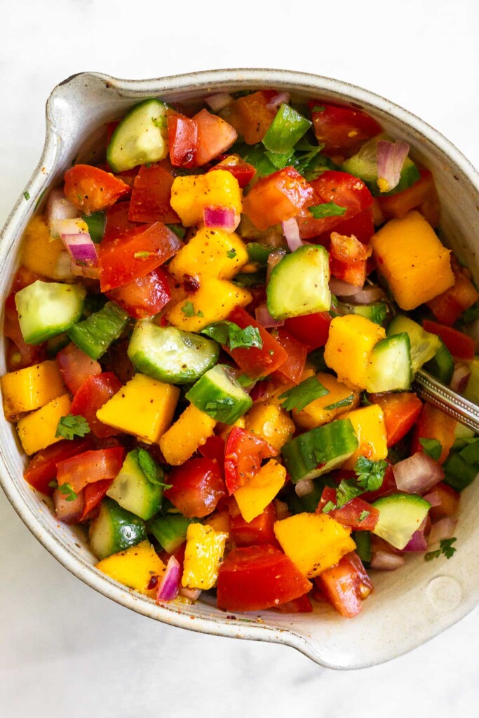 A close up of a bowl of fresh mango salsa with cucumber, tomatoes, red onion, jalapeño, cilantro, and spices.