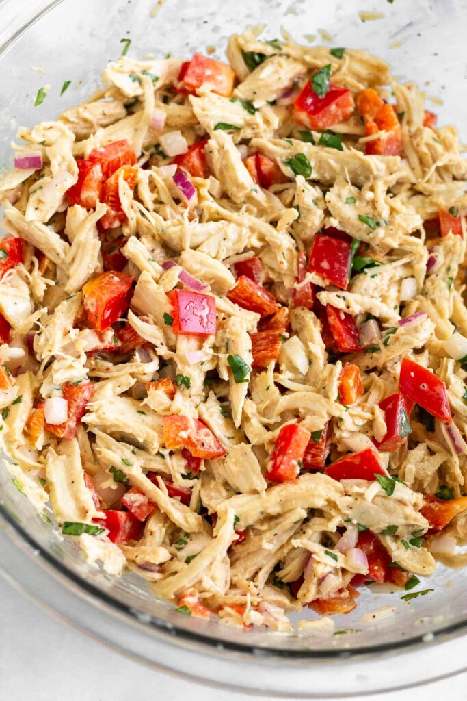 A bowl of shredded chicken mixed with bell peppers, diced red onion, and cilantro tossed in a light dressing.