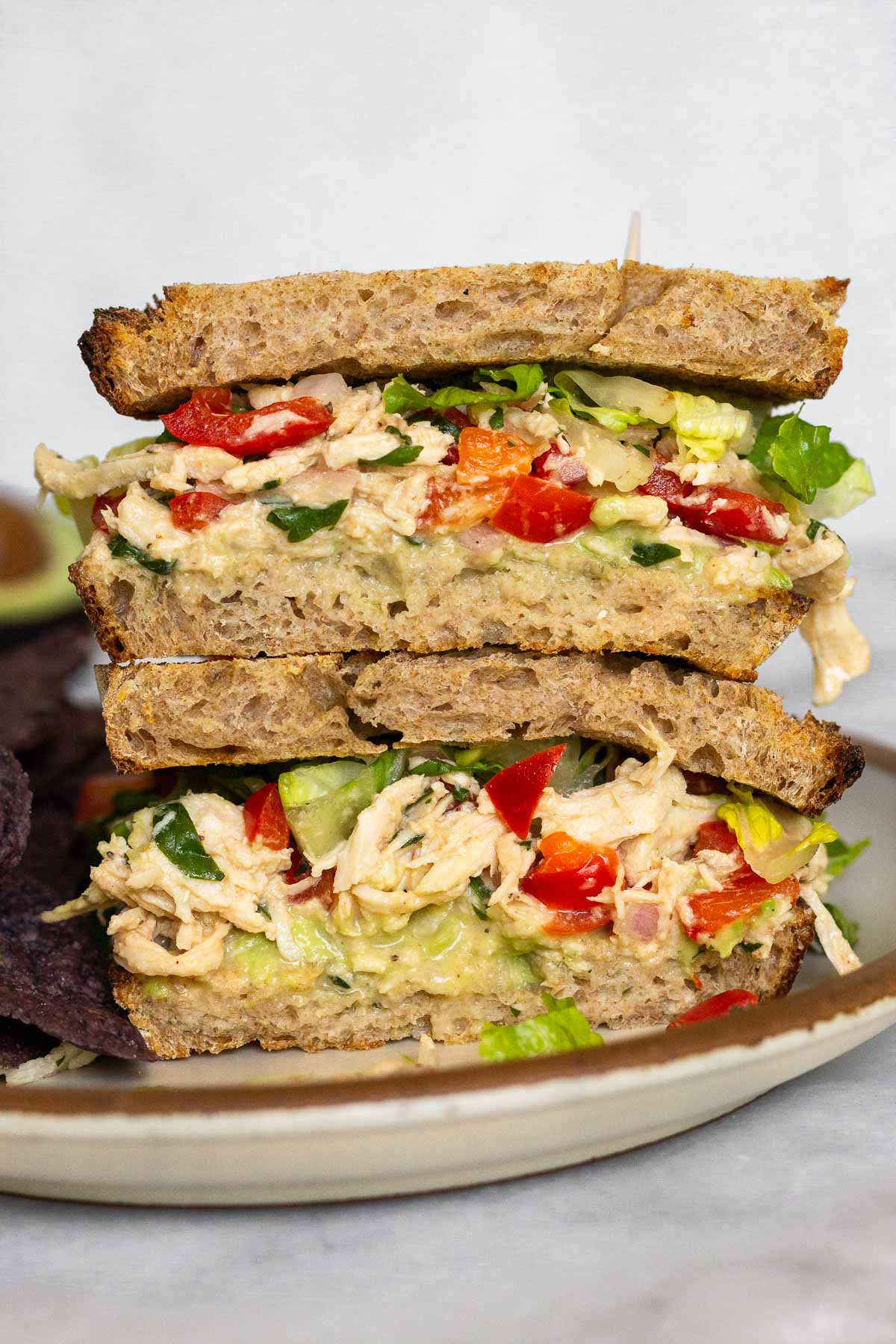 Two halves of a chipotle chicken salad sandwich with lettuce and avocado stacked on top of each other on a plate.