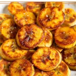 A pile of fried sweet plantains on a white plate. They are garnished with flaky salt.