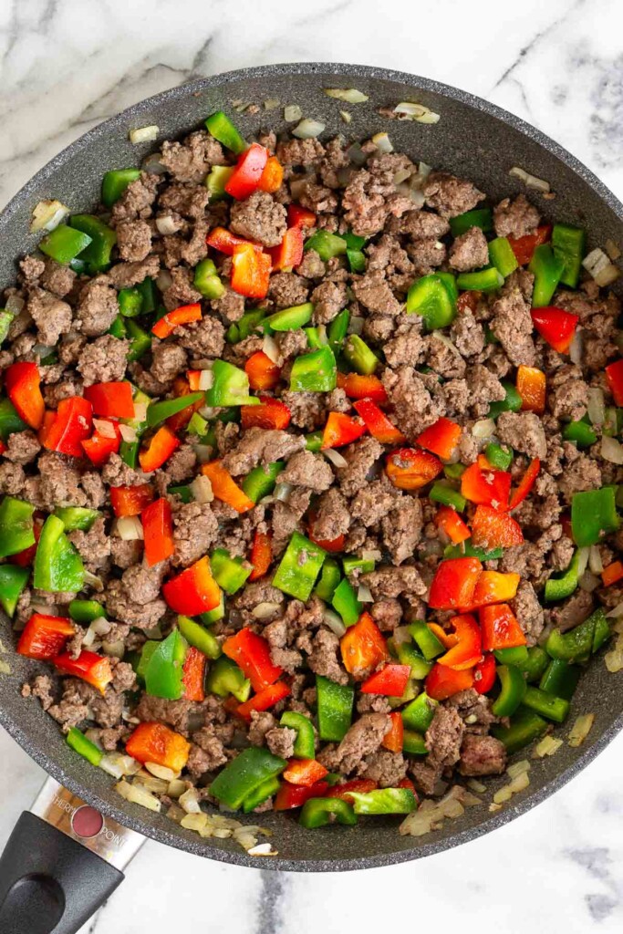 Large sauté pan filled with sautéed ground beef, diced onions, and diced bell peppers.