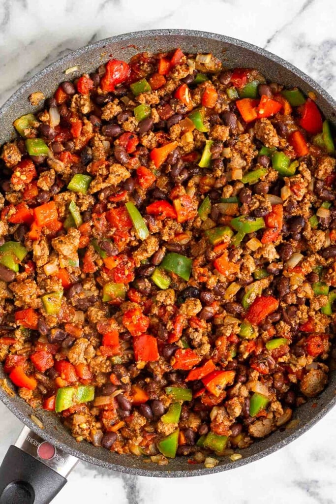 Large sauté pan filled with a mixture of sautéed ground beef, diced bell peppers, black beans, and fire roasted tomatoes.