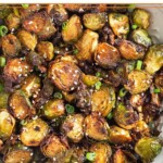 Large white bowl filled with crispy air fryer brussel sprouts garnished with sesame seeds and green onions.