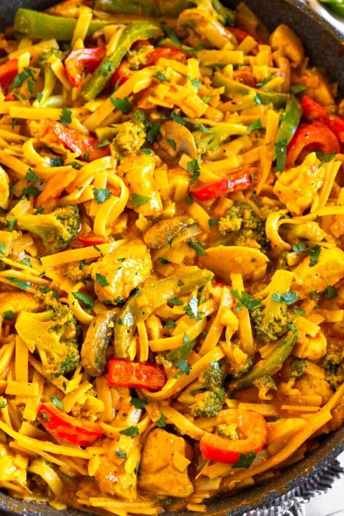 Thai curry noodles with chicken and veggies in a pan. It is garnished with fresh cilantro.