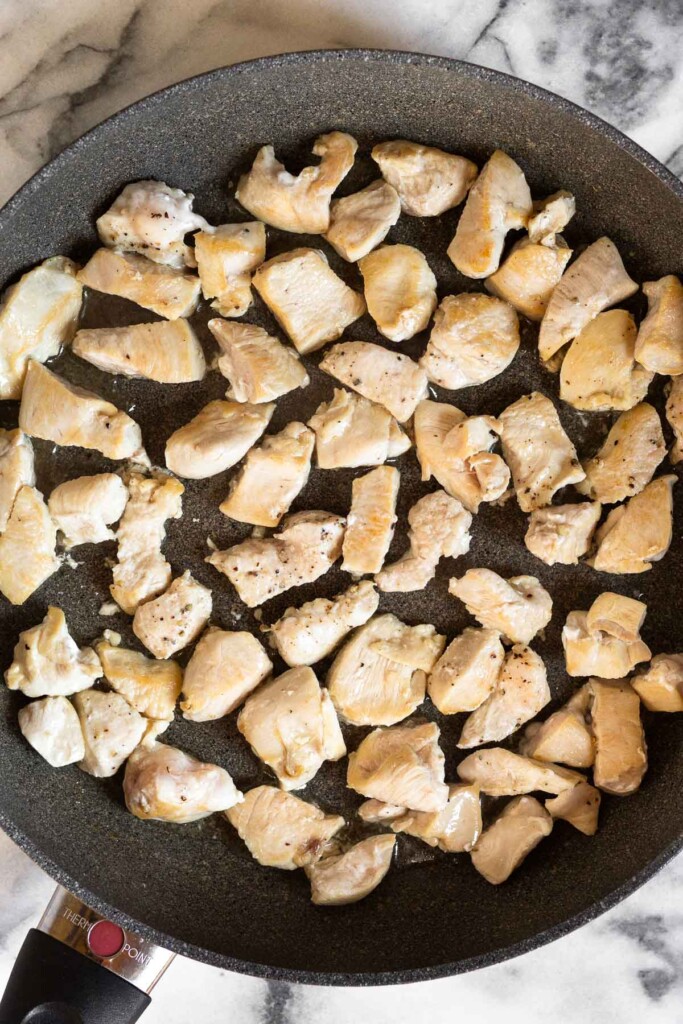 Large skillet filled with bite sized pieces of sautéed chicken.