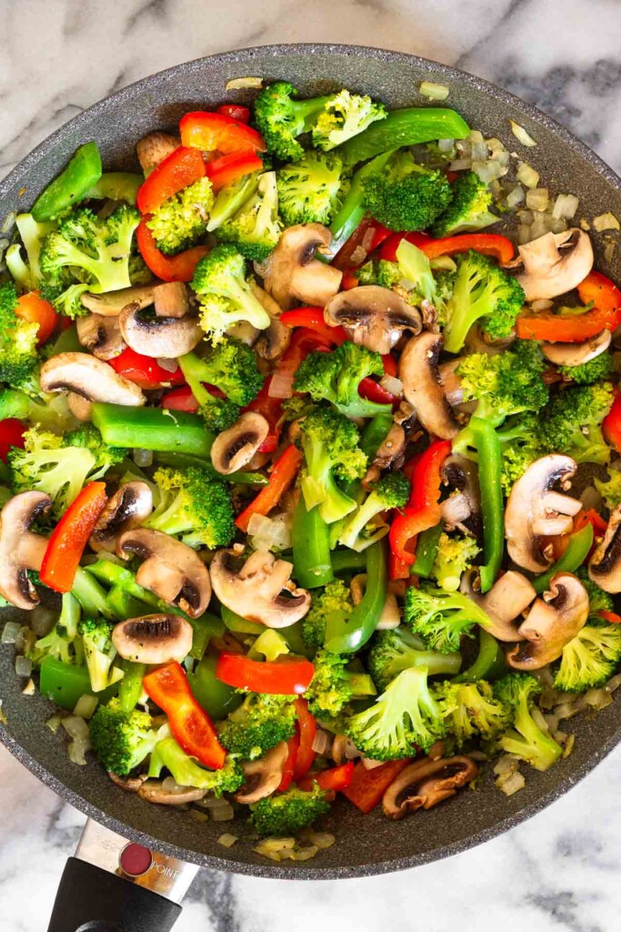 Large skillet filled with sautéed onions, mushrooms, bell peppers, and broccoli.