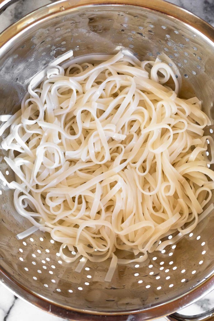 Overhead shot of a colander with cooked rice noodles in it.