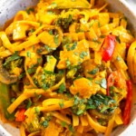 A close up of curry noodles with chicken and veggies in a white bowl topped with cilantro.