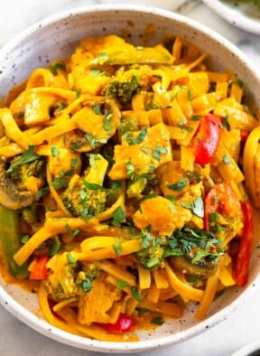 A close up of curry noodles with chicken and veggies in a white bowl topped with cilantro.