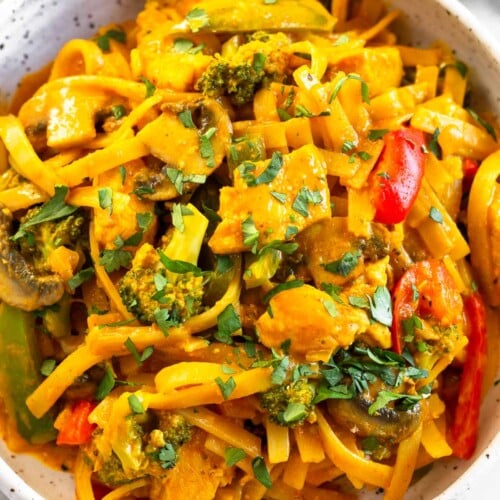 A close up of curry noodles with chicken and veggies in a white bowl topped with cilantro.