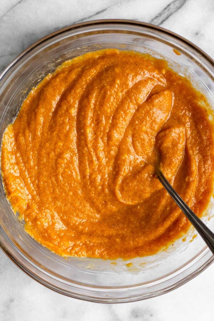 A glass bowl with a wet pumpkin batter with a fork in it.
