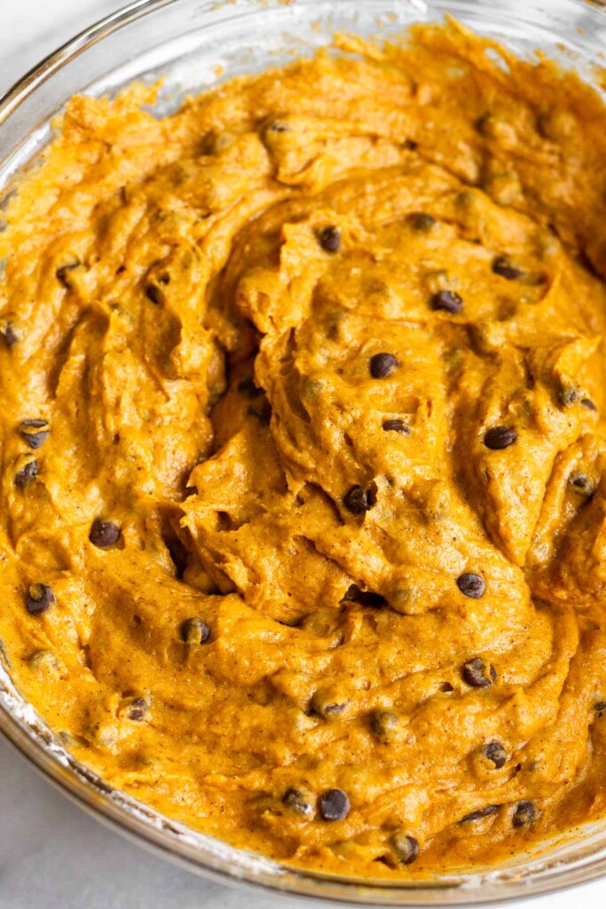A close up shot of a thick muffin batter with mini chocolate chips in a glass bowl.