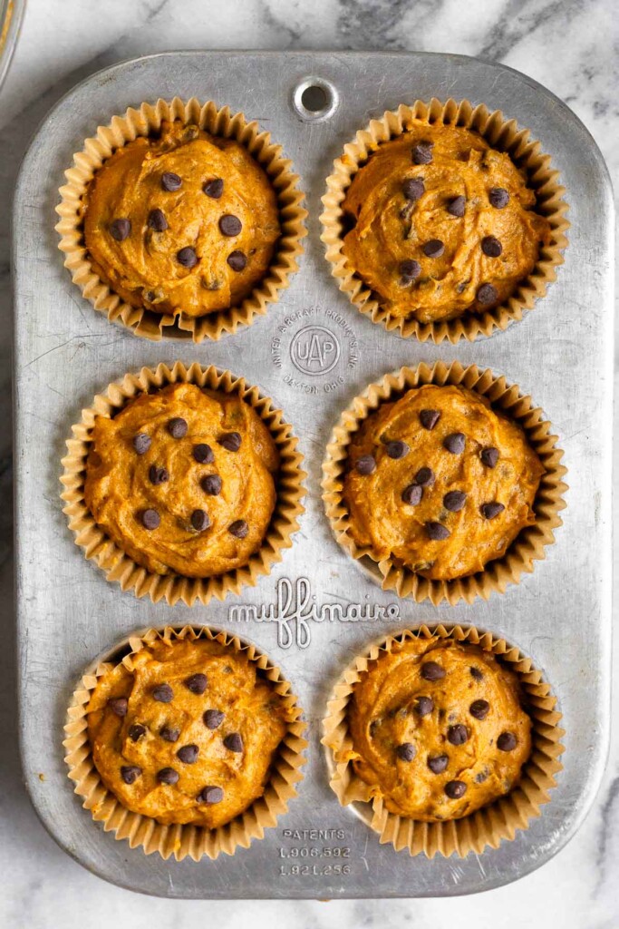 Muffin tin with muffin liners filled with uncooked muffin batter with chocolate chips in it.