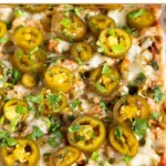 A close up of cheesy sausage dip topped with pickled jalapeños and cilantro in a glass baking dish.