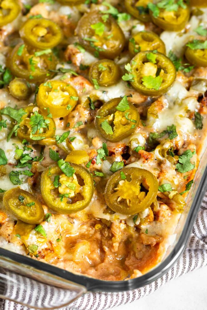 Sausage bean dip topped with pickled jalapeños in a glass baking dish with a scoop taken out of it.