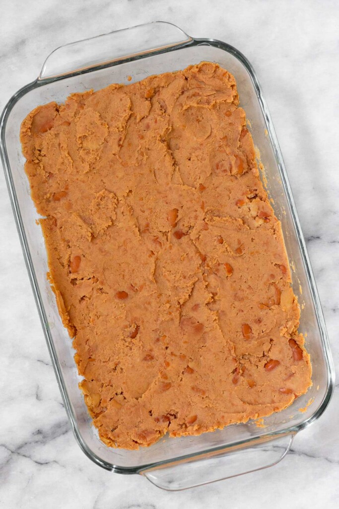 Overhead shot of a glass baking dish with refried beans evenly spread across the bottom.