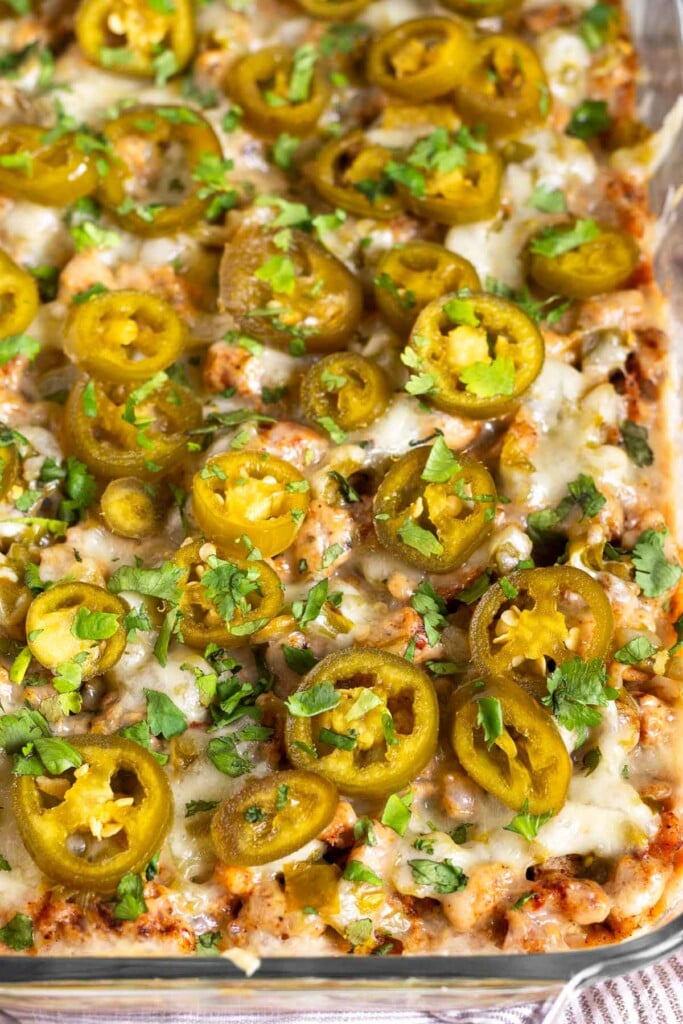 A close up of sausage cheese dip topped with pickled jalapeños and cilantro in a glass baking dish.