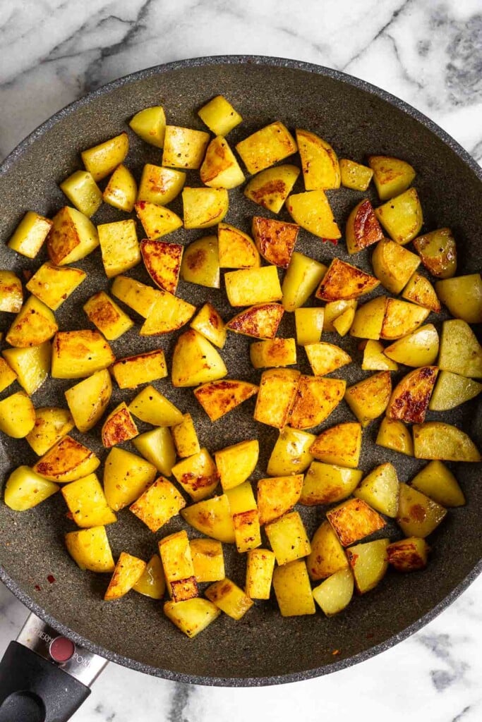 Large skillet filled with sautéed diced potatoes.